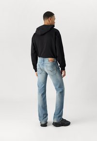 Sweatshirt com capuz preto emparelhado com jeans de tom azul claro. Os jeans apresentam denim desbotado, bolsos traseiros e uma etiqueta castanha na cintura. Ténis pretos.