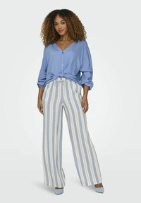 Blauwe blouse met knoopdetail aan de voorkant, gecombineerd met wijde gestreepte broek in lichtblauw en crèmekleur. Gladde stof en relaxte pasvorm.