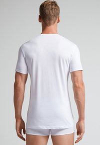 Camiseta blanca de manga corta, material de algodón, forma ajustada, textura suave, sin patrones ni diseños, vista desde atrás.