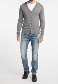 Cardigan grigio con scollo a V, chiusura con bottoni e polsini a coste, abbinato a jeans azzurri chiari e sneakers nere. Outfit semplice e casual.