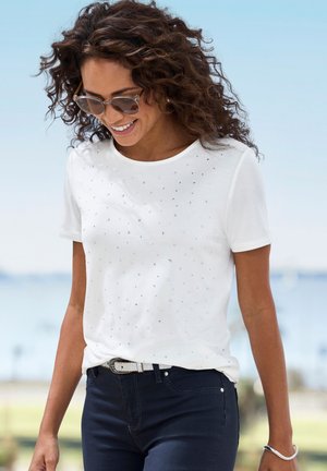 White cotton t-shirt with short sleeves, featuring scattered rhinestones on the front. Paired with dark blue jeans and a light belt.