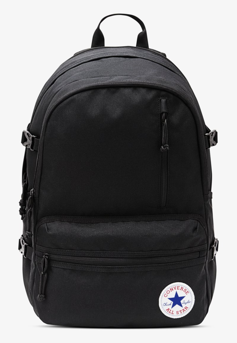 Sort stofrygsæk med flere lynlåslommer, justerbare stropper og et rundt Converse-logo nederst. Grundlæggende rektangulær form.
