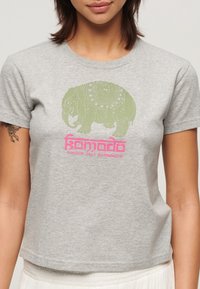 Grå bomuld t-shirt med et lyst grønt elefantgrafik og pink tekst, der står "Komodo London Dali Kathmandu." Kortærmet med rund hals.