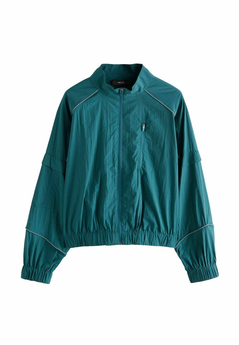Giacca leggera color teal con colletto alto, polsini e orlo elasticizzati. Presenta passamaneria argentata lungo le cuciture e una tasca sul petto con cerniera.