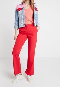 Pantalones rojos ajustados con un corte recto, combinados con una chaqueta de mezclilla en tonos rosa y azul y una camiseta coral, completados con zapatillas blancas.