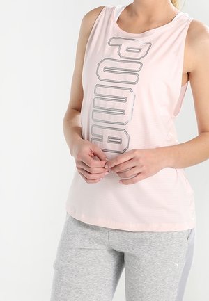 Femme portant un débardeur Puma rose clair et un pantalon de sport gris clair sur fond blanc uni.