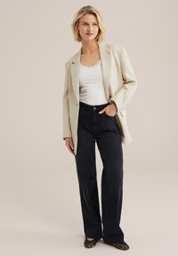 Béžový blazer, biely top bez rukávov a tmavé džínsy; leopardie vzorované baleríny. Blazer má voľný strih, s jedným gombíkom a vreckom.