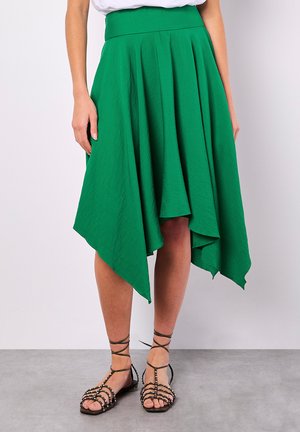 Groene asymmetrische rok met plooien, gemaakt van lichte stof, met een gladde textuur en een vloeiende silhoutte. Aangevuld met sandalen met bandjes.