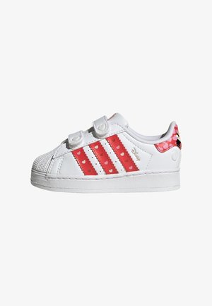 White sneakers with red detailing, featuring three stripes with heart patterns, Velcro straps, and a textured toe cap design.