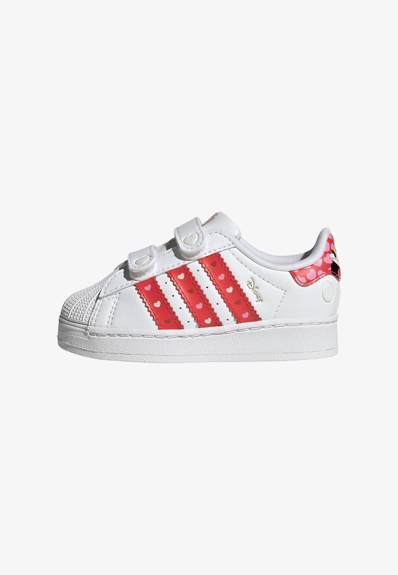 Des baskets blanches avec des détails rouges, ornées de trois rayures avec des motifs en forme de cœur, des sangles Velcro et un design de coque de orteils texturée.
