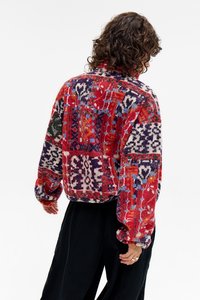 Fleece pulover u crvenoj i ljubičastoj boji sa uzorkom, labavog kroja, stojećim ovratnikom i oversized rukavima, koji prikazuje složene dizajne i mekanu teksturu.