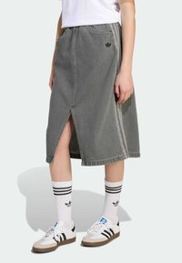 Lys grå denimskjørt med en frontsplitt, akkompagnert av en liten svart logo, kombinert med hvite sokker med svarte striper og klassiske sneakers.