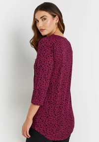 Top fucsia con motivo floreale nero, maniche a tre quarti e un orlo curvo, realizzato in tessuto morbido e leggero.