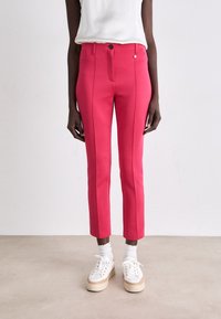Slim-fit, felroze broeken met een soepele textuur, sluiting met een knoopsysteem aan de voorkant en zijnaad. Gecombineerd met witte sneakers en geribbelde sokken.