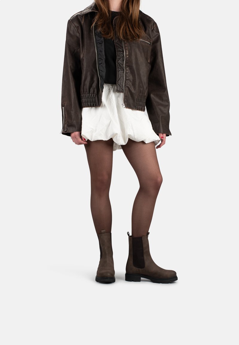 Bruine leren bomberjack, witte gerimpelde shorts, doorschijnende panty’s en bruine enkelaarsjes met elastische zijkanten. Eenvoudig, modern ontwerp.