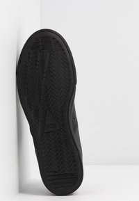 Black sneaker sole with textured tread pattern. Smooth upper edge with rounded shape and reinforced toe. Triangle branding detail present.