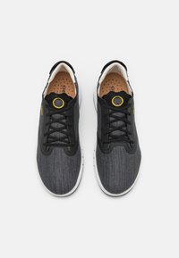 Zapatillas de tela negras con un acabado texturizado, cordones redondos, acento amarillo y suela de goma blanca. Incluyen una plantilla acolchada con perforaciones.