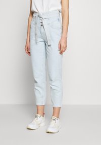 Ljust blå högmidjade jeans med framfickor, hällor och ett tygskärp; matchade med vita sneakers med gula detaljer.