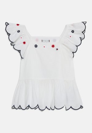 Hvitt ermeløst topp med bølgete kanter, svart kanting og små røde og svarte blomsterbroderier på skuldrene og i halsen.