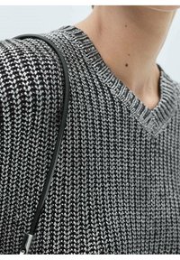 Musta-valkoinen neulottu villapaita V-pääntiellä ja tekstuurillisella kuviolla, jossa on ohut musta hihna ja hopeiset metalliset yksityiskohdat.