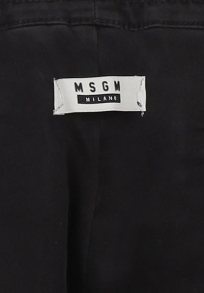 Etichetta in tessuto nero con la scritta "MSGM MILANO" stampata in bianco e nero. Etichetta attaccata a un capo di abbigliamento, con bordi dritti e cuciture visibili.