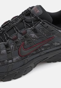 Calçado Nike com um cabedal texturizado em preto e cinza, detalhes em vermelho e um design de sola distinto. Possui um sistema de aperto para garantir um ajuste seguro.
