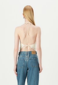 Krémový halter top s čipkovým lemovaním a viazaním na chrbte; spárovaný s vysokými modrými džínsami s hnedou koženou nášivkou na páse.