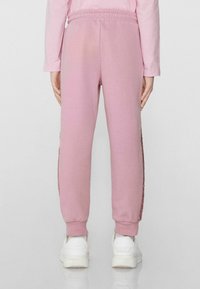 Rosa Sweatpants mit elastischem Bund, gerippten Ärmelbündchen und seitlichen Details. Kombiniert mit weißen Schuhen für einen lässigen Look.