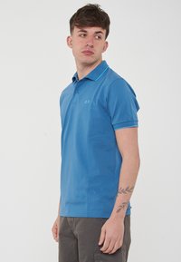 Polo shirt blu in cotone con un design semplice, patta con tre bottoni e dettagli turchesi a contrasto sul colletto e sulle maniche.