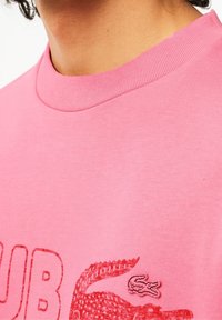 T-shirt en coton rose avec un col rond côtelé et un logo texturé rouge de crocodile sur le devant.