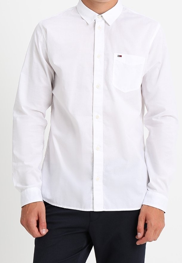 Camisa blanca de manga larga con cuello, cierre frontal con botones y un bolsillo en el pecho con un pequeño logo en el mismo. Tejido de algodón suave.