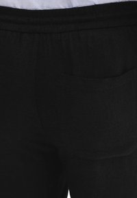 Czarne spodnie wykonane z teksturowanej tkaniny, z małą tylną kieszenią oraz elastycznym pasem dla wygody.