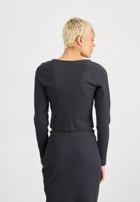 Mørkegrå ripet langermet kort topp med rund hals og tettsittende silhuett. Stoffet viser fine vertikale linjer og har en sømløs finish.