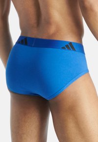 Blå sportskalsonger med en solid textur, utrustade med ett svart elastiskt midjeband med tre svarta ränder och logotypdetalj på baksidan.