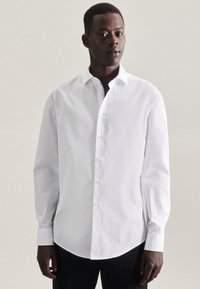 Chemise blanche à manches longues en tissu lisse, dotée d'un col classique et d'un ourlet arrondi. Boutons le long du devant.