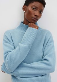 Maglione lavorato a maglia di colore azzurro chiaro con colletto alto, polsini a coste e vestibilità rilassata. Tessuto morbido con un design pulito e minimalista.