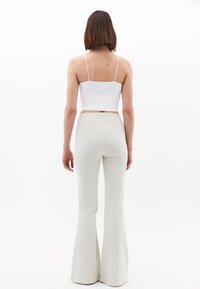 Vit korta linne med tunna axelband, matchat med ljusgrå, figurnära utsvängda byxor. Slät textur, minimalistisk design, elegant silhuett.