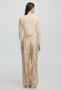 Maglione a maniche lunghe con texture cremosa e design a coste, abbinato a pantaloni larghi di tonalità dorata con un sottile motivo floreale.