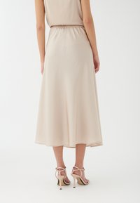 Vestido midi de color beige claro con cinturilla elástica, tejido fluido y dobladillo a la altura de la rodilla. Combinado con sandalias de tacón alto con tiras.