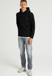 Sudadera negra con bolsillo frontal y cordón, llevada sobre una camiseta blanca. Combinada con jeans de mezclilla azul claro y zapatillas grises.