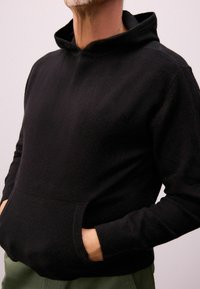 Sort fleece hættetrøje med en frontlomme, lange ærmer og høj krave. Blød tekstur med manchetter og kant afsluttet i en matchende strik.