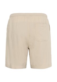 Beige cotton shorts with an elastic waistband, a single back pocket, and a relaxed fit. Smooth texture, mid-thigh length.