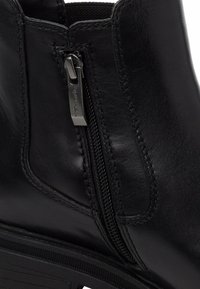 Black leather ankle boot featuring a side zipper, stitched accents, and a ridged rubber sole for traction. Smooth texture throughout.