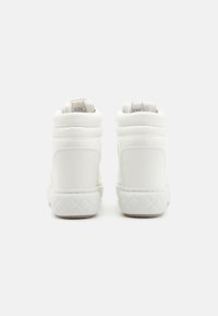 Baskets montantes blanches en matériau synthétique lisse, avec des accents matelassés sur le talon et une semelle en caoutchouc texturé conçue pour l'adhérence.