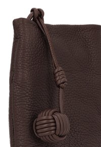 Bolso de cuero marrón con textura y cierre de nudo, presenta un acabado liso y un detalle de nudo redondeado cerca de la apertura.