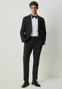 Tuxedo nero con un sottile motivo testurizzato, rever in satin, camicia bianca, papillon nero e scarpe eleganti nere lucide.