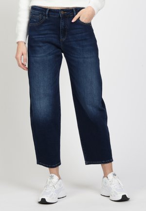 Dark blue denim jeans with a relaxed fit, five-pocket design, and a straight leg. Worn with white athletic sneakers.