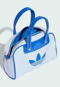 Niebiesko-biała torba z lakierowanej skóry, z dwoma niebieskimi uchwytami, zapięciem na zamek i dużym niebieskim logo Adidas trefoil na przodzie.