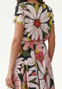 Blomstret kjole med store hvide og lyserøde blomster samt grønne blade mod en sort baggrund. Korte ærmer, indsnævret talje og plisseret nederdel.