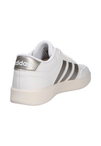 Vit sneaker med silverdetaljer, med en slät läderöverdel, tre svarta ränder och en texturerad gummisula. Minimalistisk design.